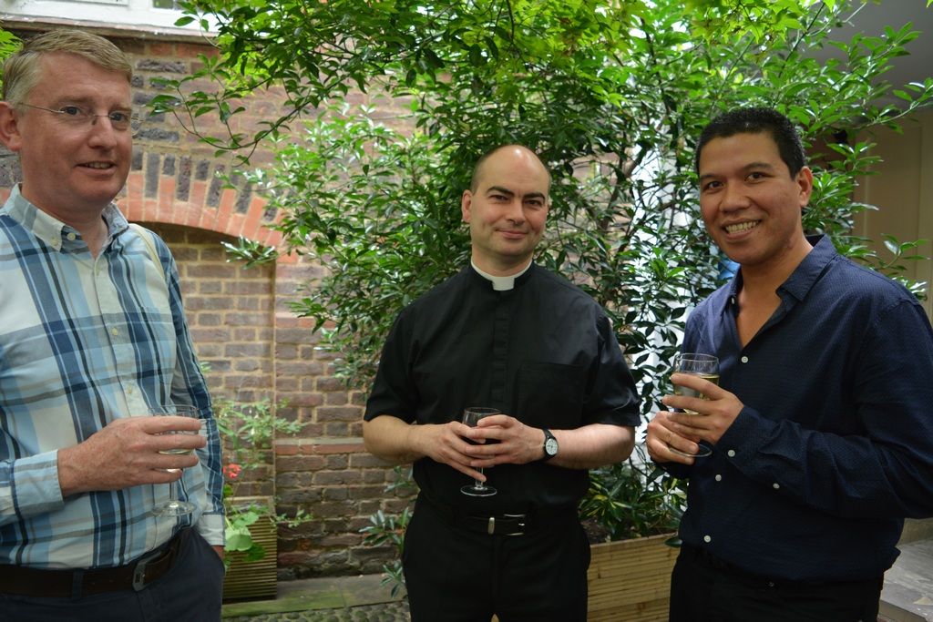 Three guests chatting with drinks beside the courtyard wall.