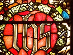 A close-up of stained glass with a red shield and gold ornament.