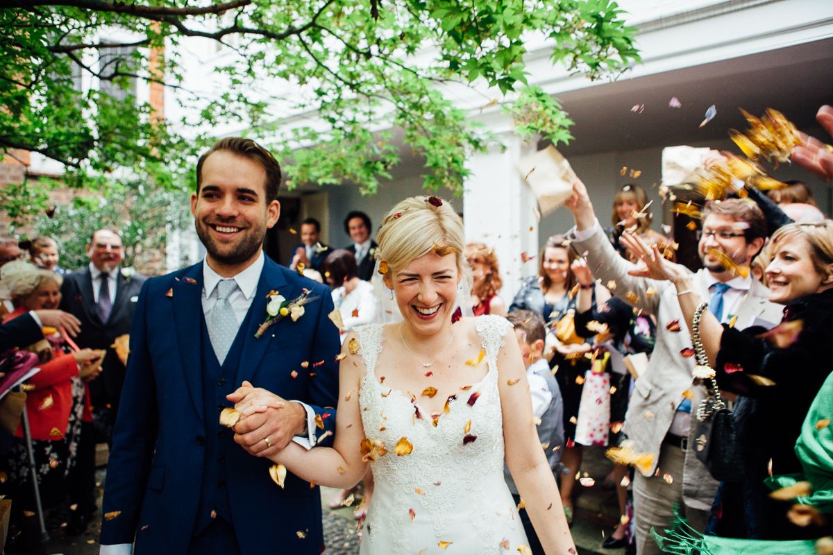 A smiling wedding couple walking through falling confetti in the courtyard.