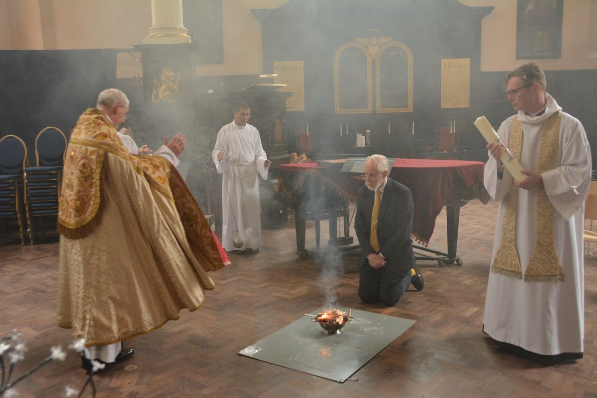 Clergy kneeling beside a small fire in the church, with smoke rising around them.