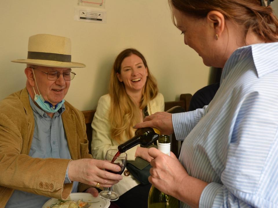 A guest pouring a drink for a seated man wearing a straw hat.
