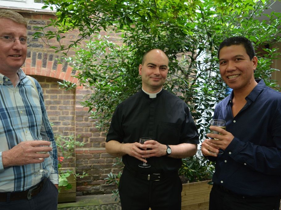 Three guests chatting with drinks beside the courtyard wall.