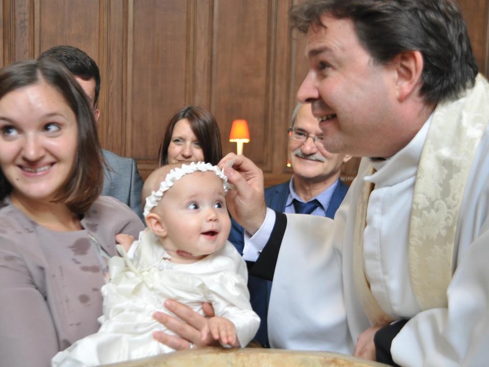 A baby held beside a priest during a baptism service.