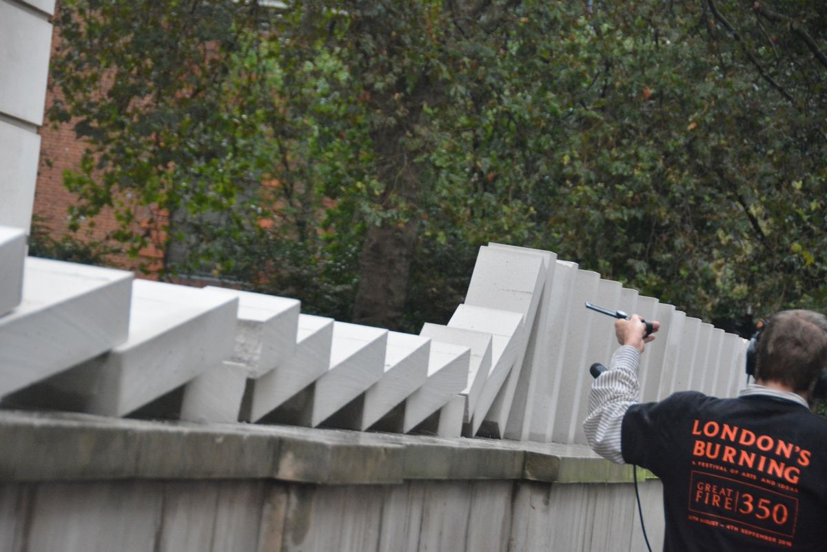 White blocks toppling along an elevated ledge beside an ivy-covered wall.