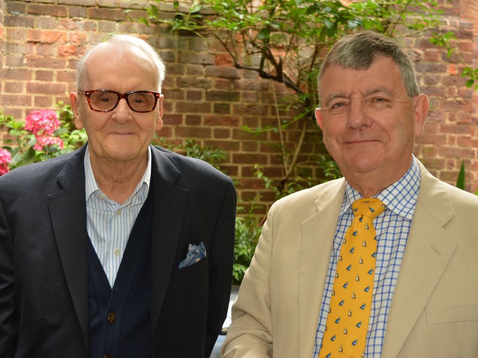 Two guests in jackets and ties standing together in the courtyard.