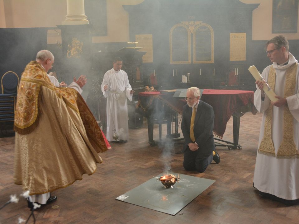 Clergy kneeling beside a small fire in the church, with smoke rising around them.