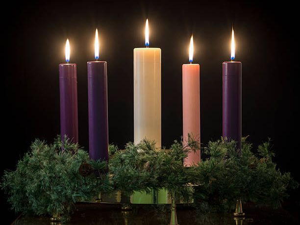 Five lit candles set in an Advent wreath against a dark background.