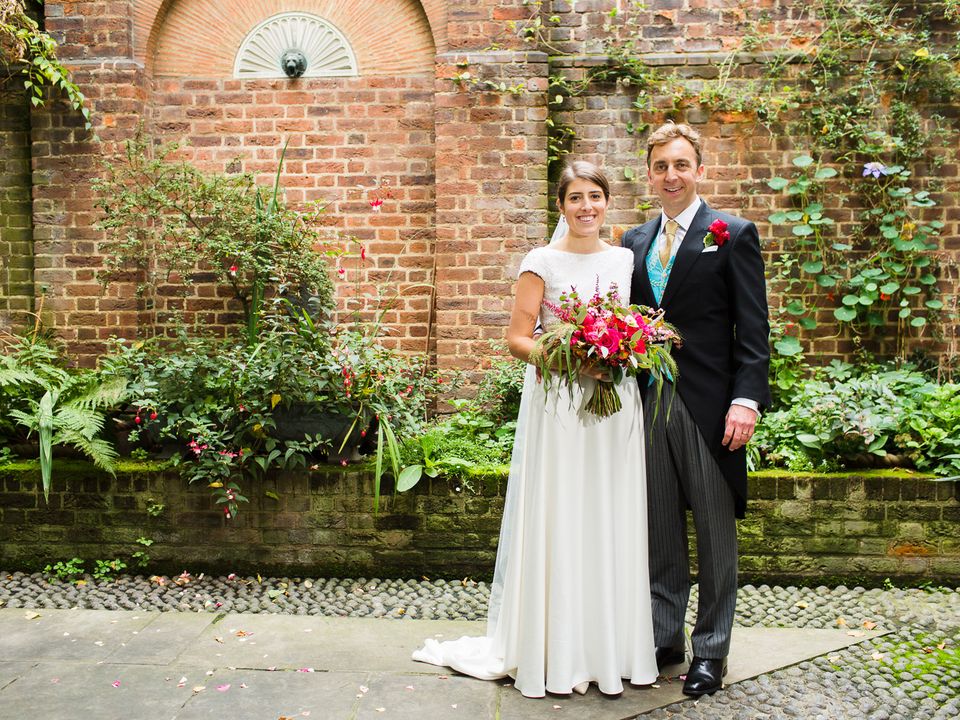 A wedding couple posing with a bouquet in the brick-walled courtyard.