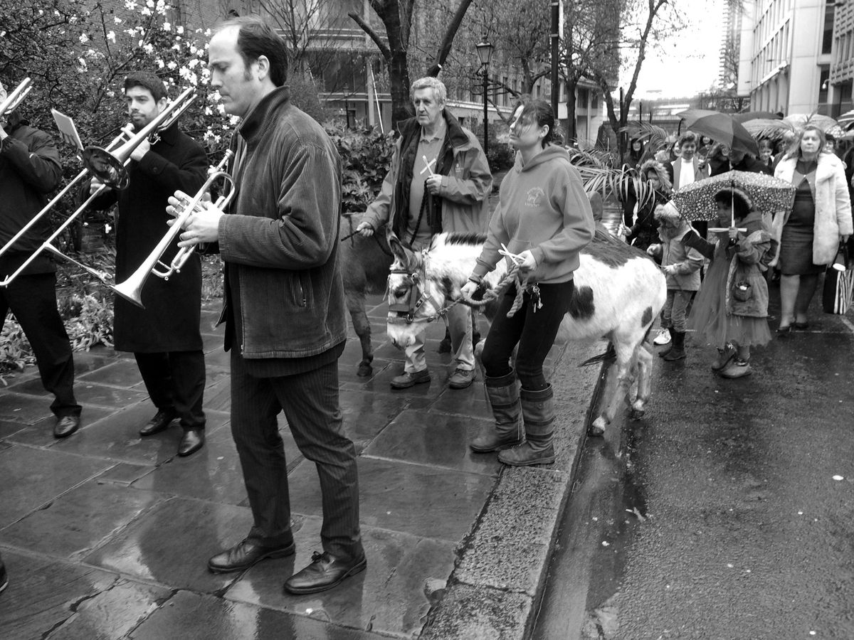 Musicians leading a procession, with a donkey and worshippers behind them.