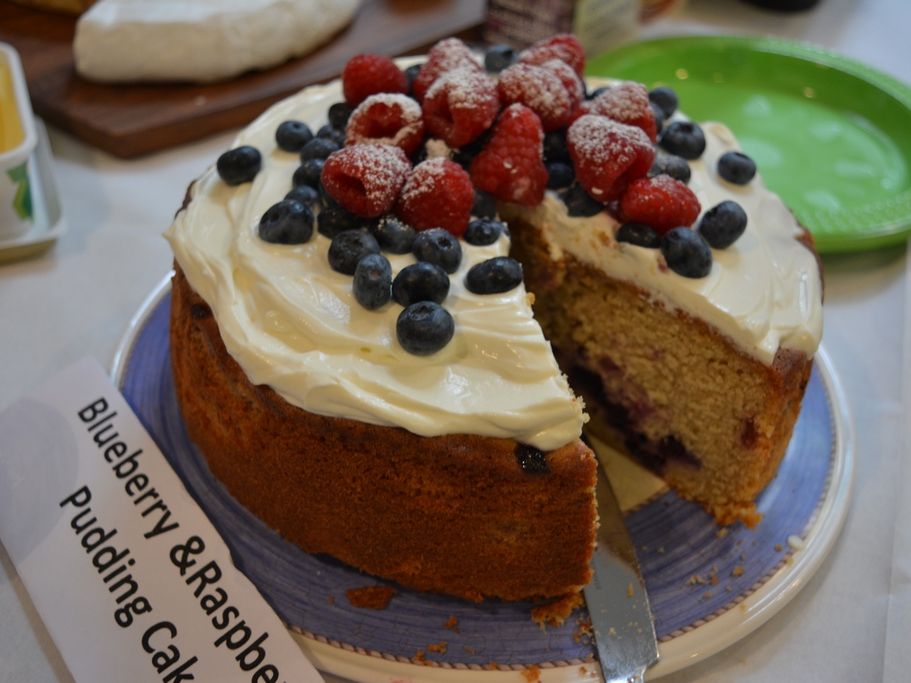 A sliced cake topped with cream, strawberries and blueberries.