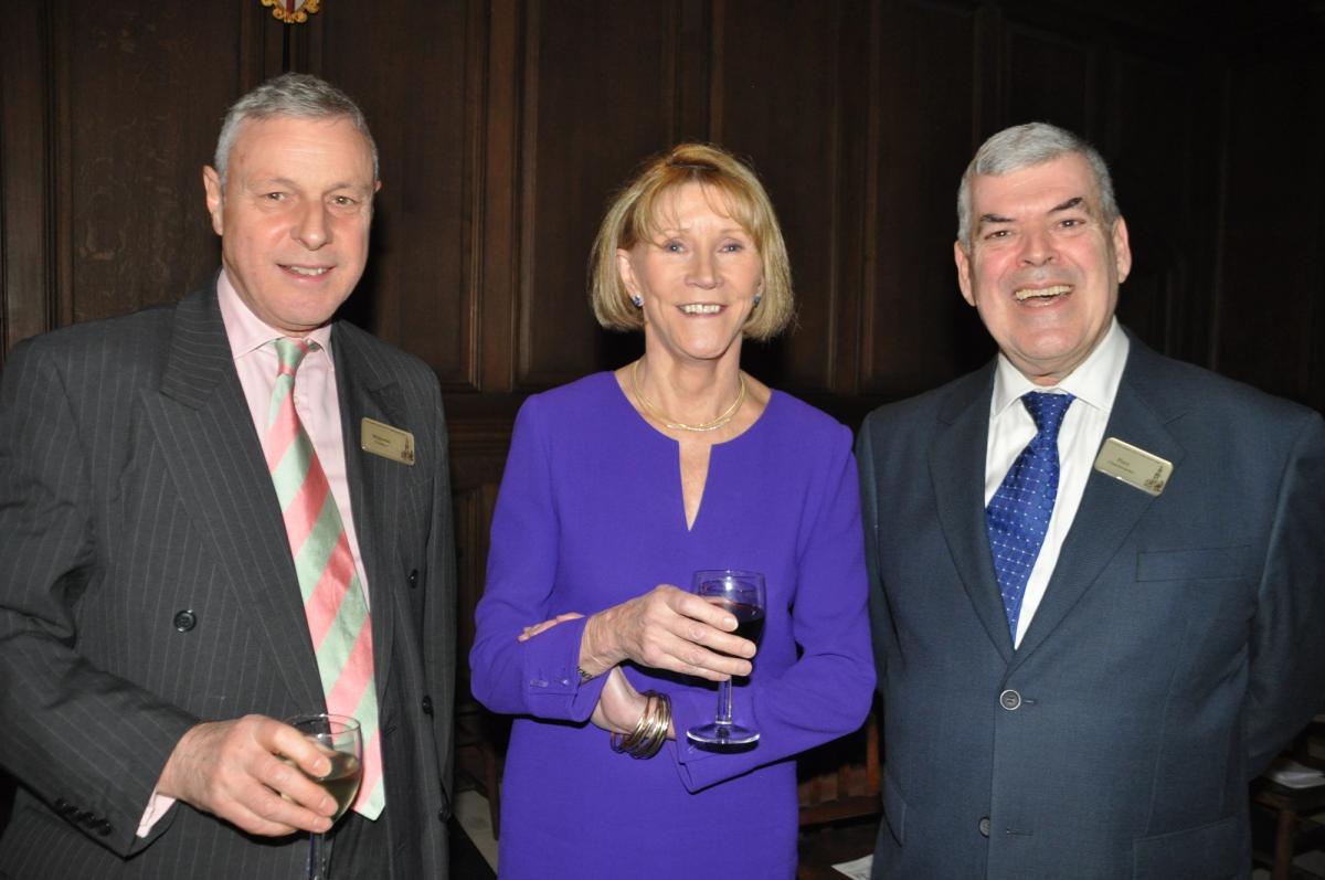 Three formally dressed guests smiling together with drinks.