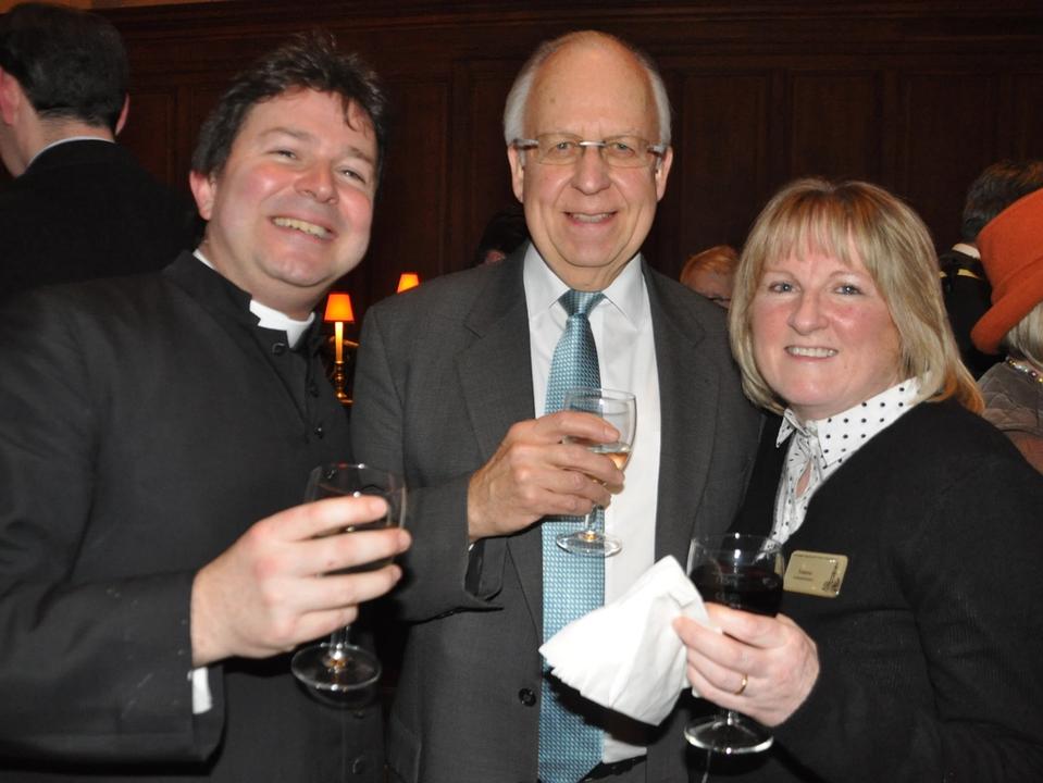 Three guests smiling and holding drinks at a church reception.