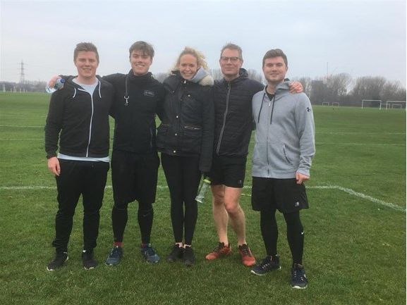 Five people standing together on a sports field.