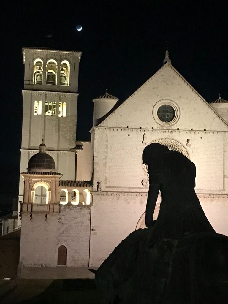 A silhouetted statue in front of a church illuminated at night.