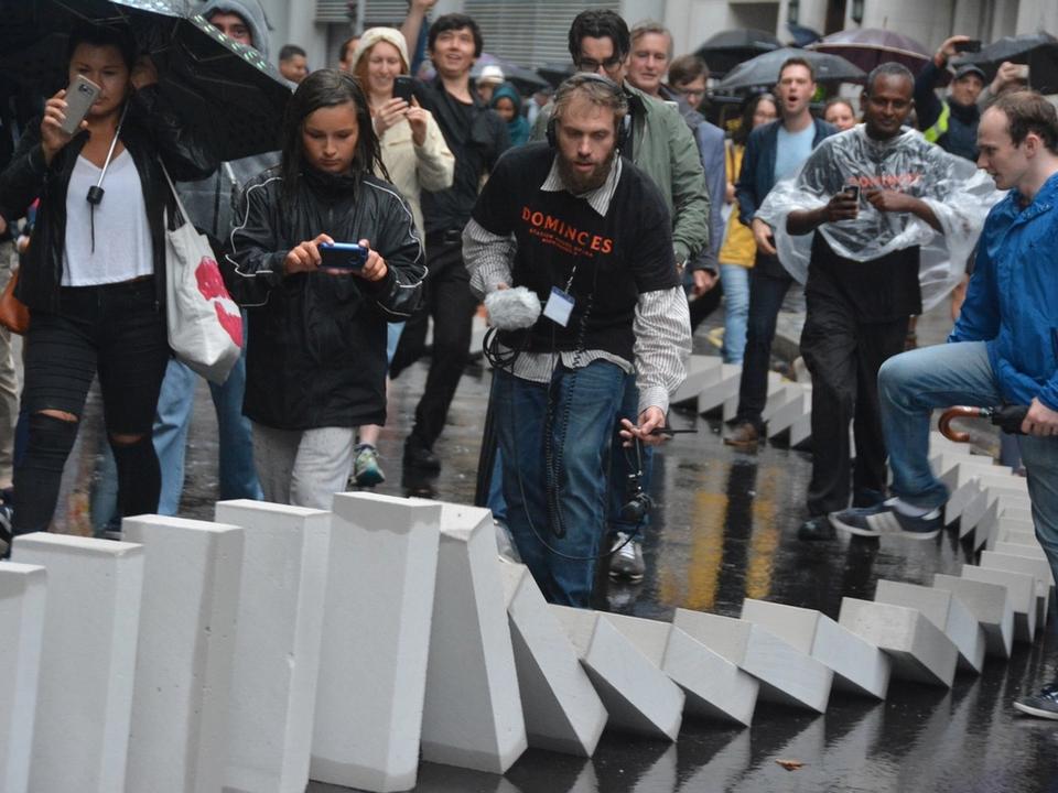 Spectators photographing a line of falling white blocks.