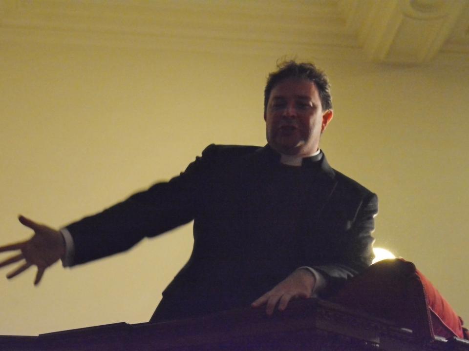 A speaker extending an arm while addressing the congregation from the pulpit.
