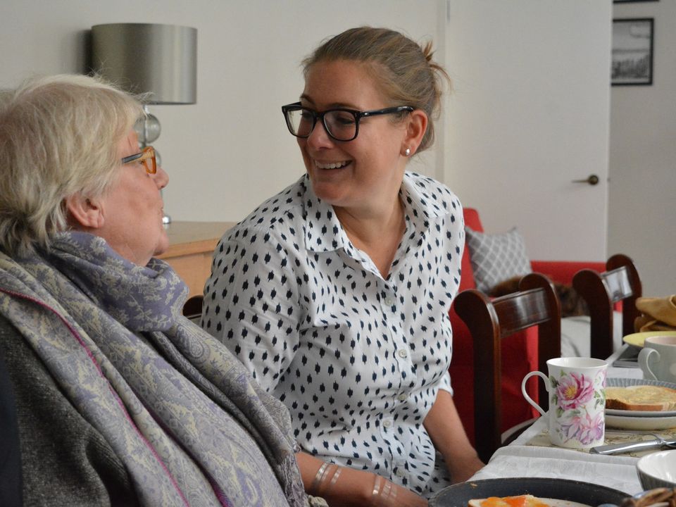 Two women chatting beside cups and plates at breakfast.