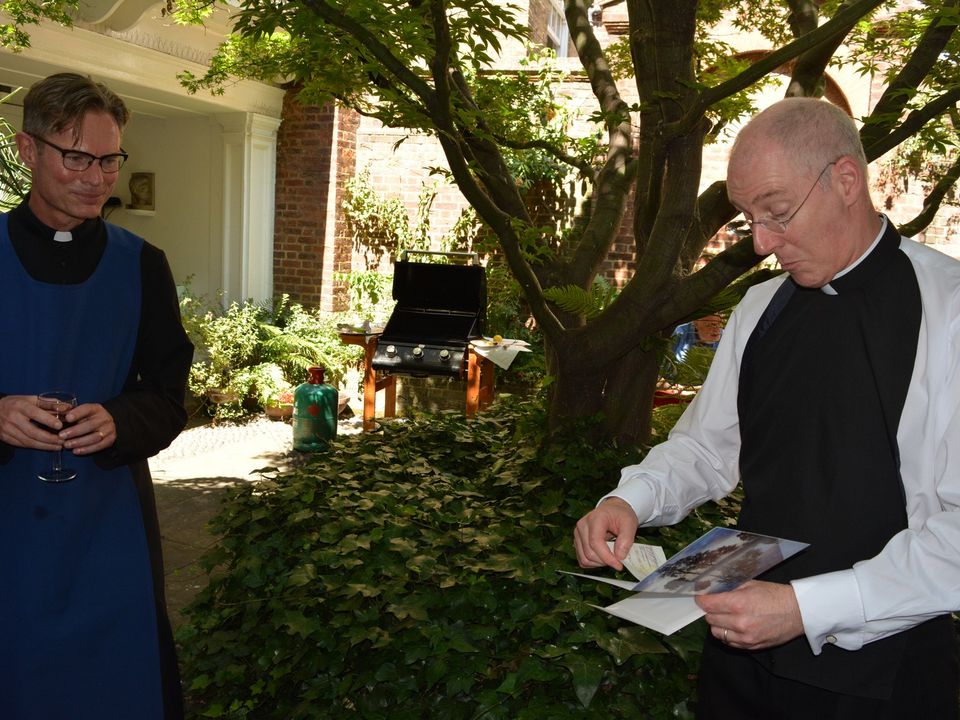 Two members of the clergy standing beside the courtyard tree.