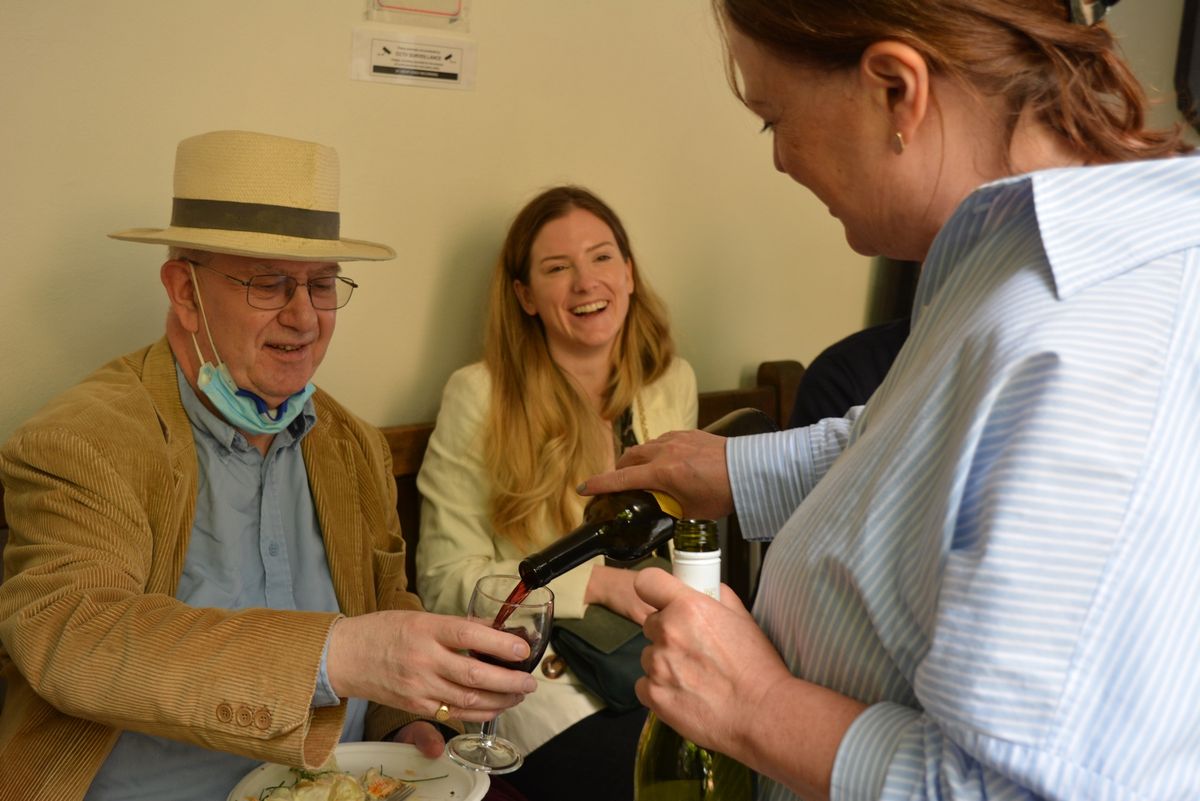A guest pouring a drink for a seated man wearing a straw hat.