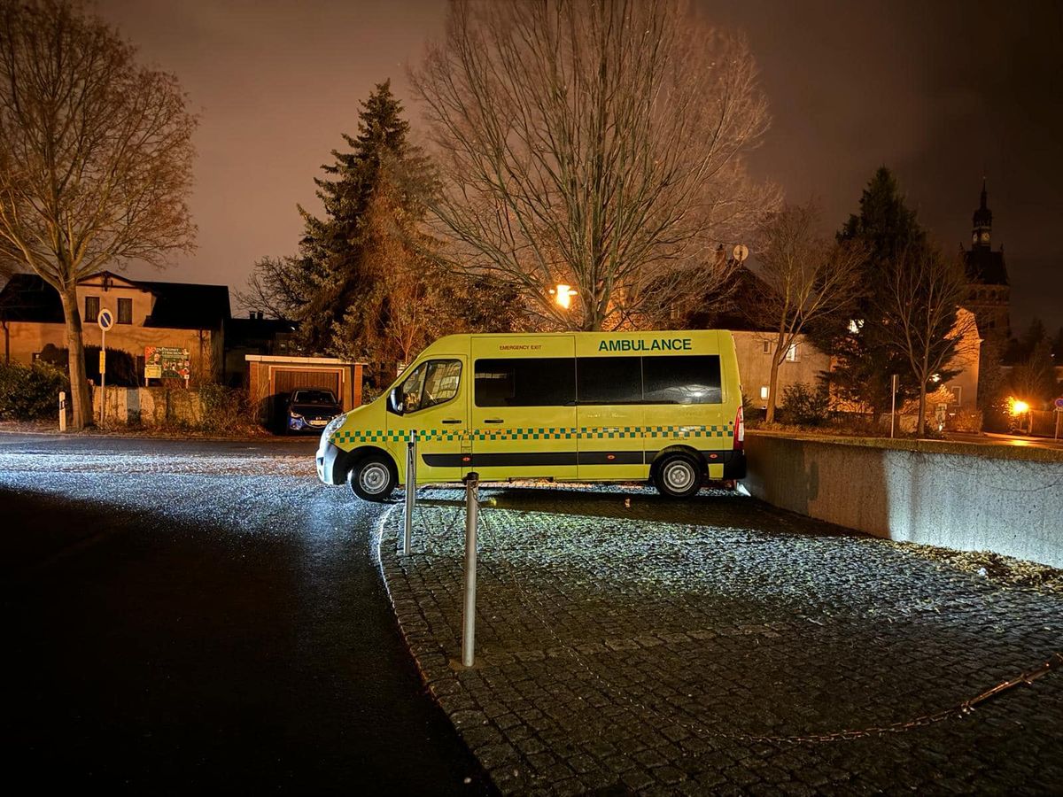 An ambulance parked outside at night beneath bare trees.