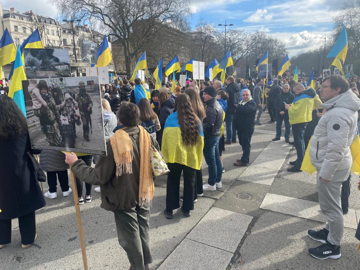 A crowd carrying Ukrainian flags at an outdoor gathering.