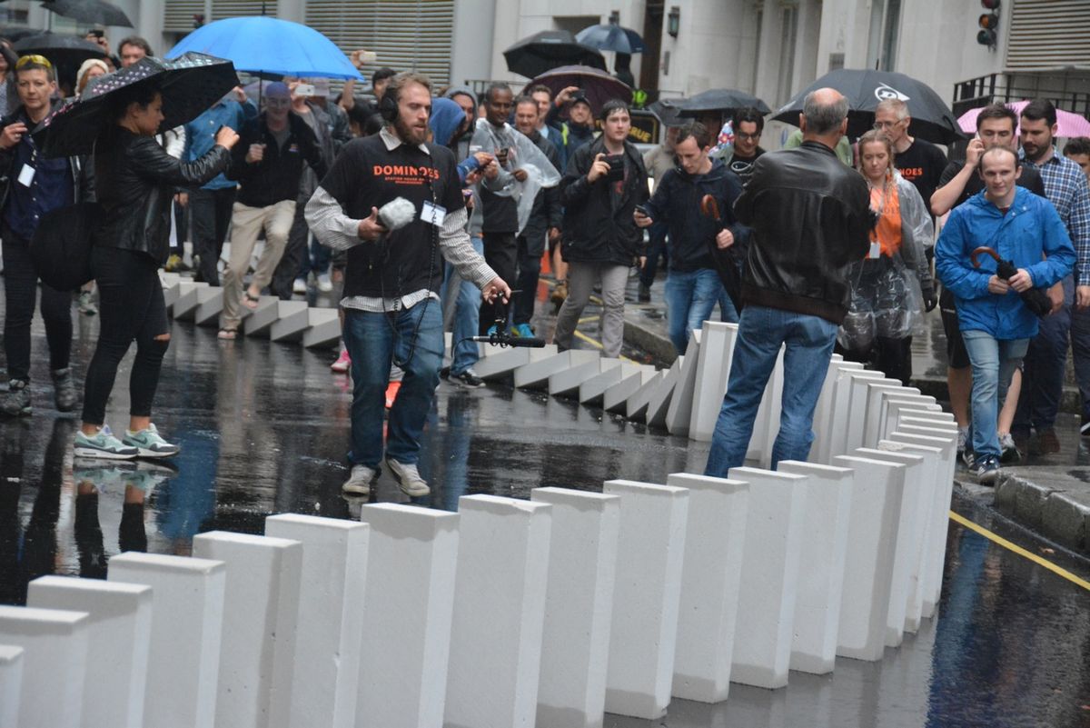A crowd watching white blocks topple along a wet street.