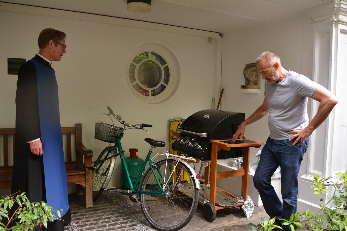 Two people beside a barbecue in the courtyard.