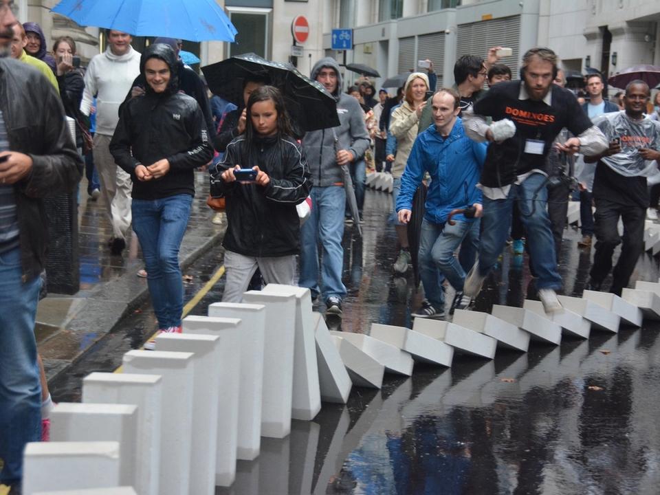People watching the white-block display fall along the pavement.