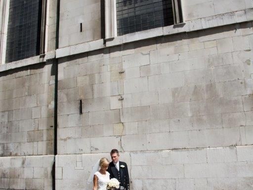 A wedding couple standing against the exterior stone wall of the church.