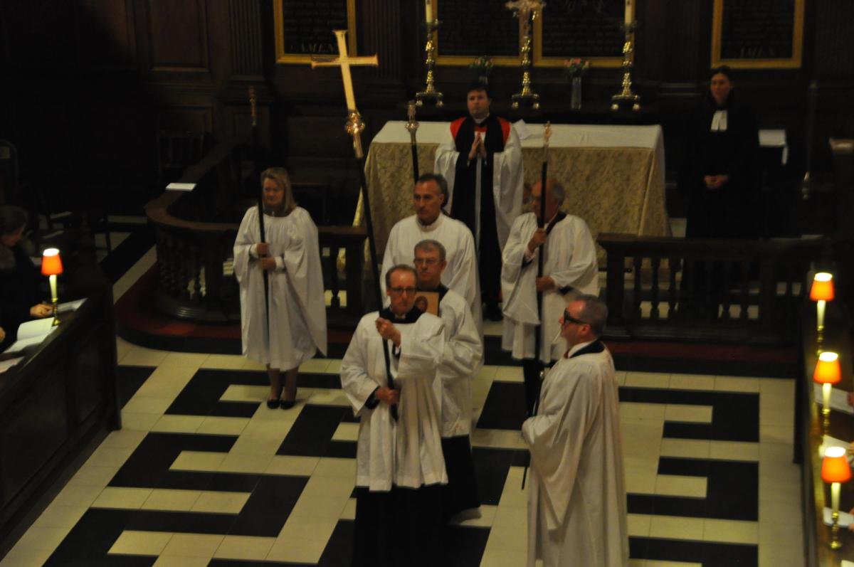 Clergy standing before the altar beneath a large processional cross.
