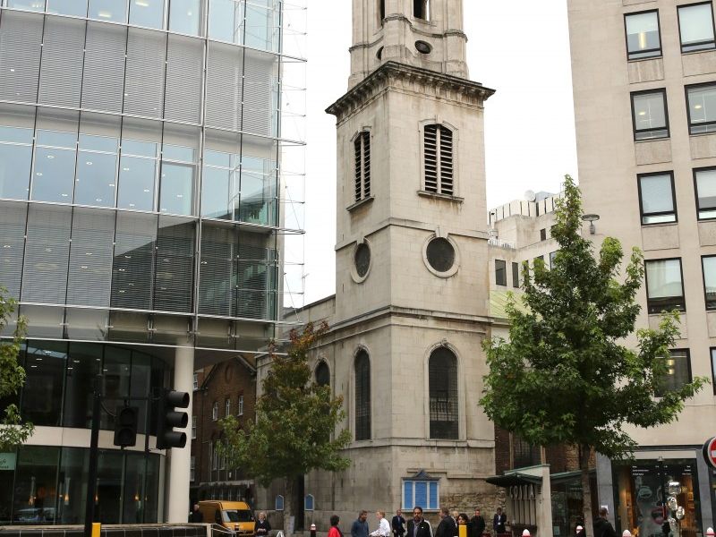 St Vedast's tower seen from across the street beside a glass-fronted building.