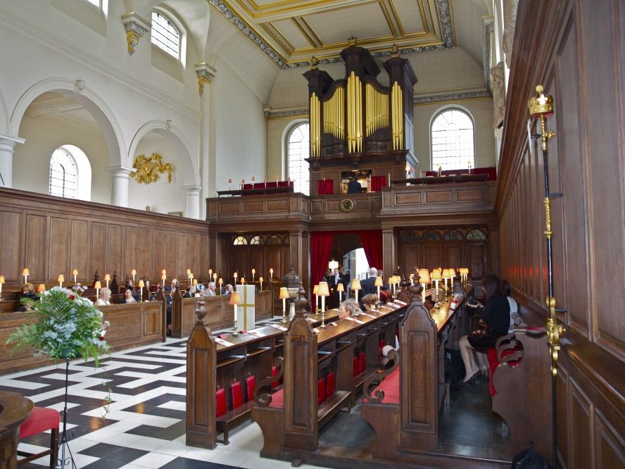The church interior, showing wooden pews, candles, patterned flooring and the organ.