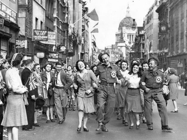 A black-and-white photograph of crowds celebrating VE Day in a London street.