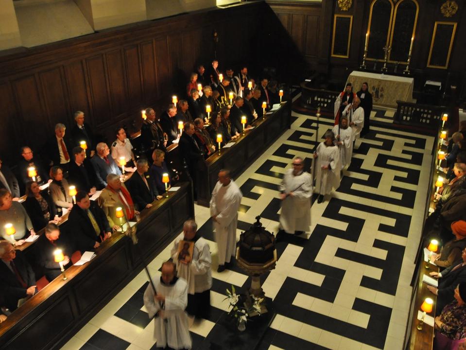 Clergy and congregation gathered around the central aisle during a candlelit service.
