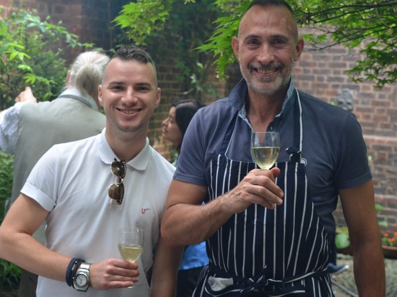 Two guests smiling with drinks beneath the courtyard tree.