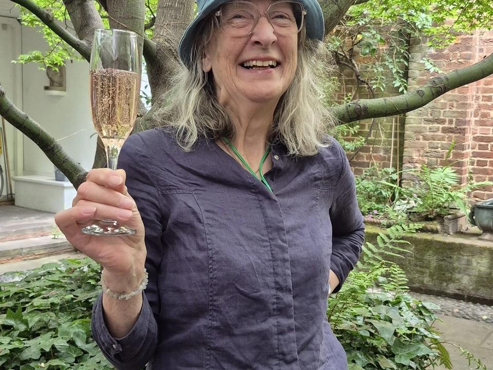 A woman in a hat raising a glass beneath the courtyard tree.