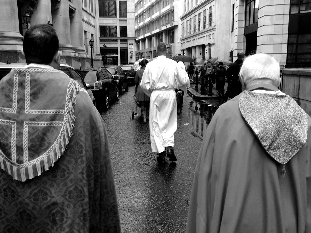 Clergy following a procession along a wet city street.