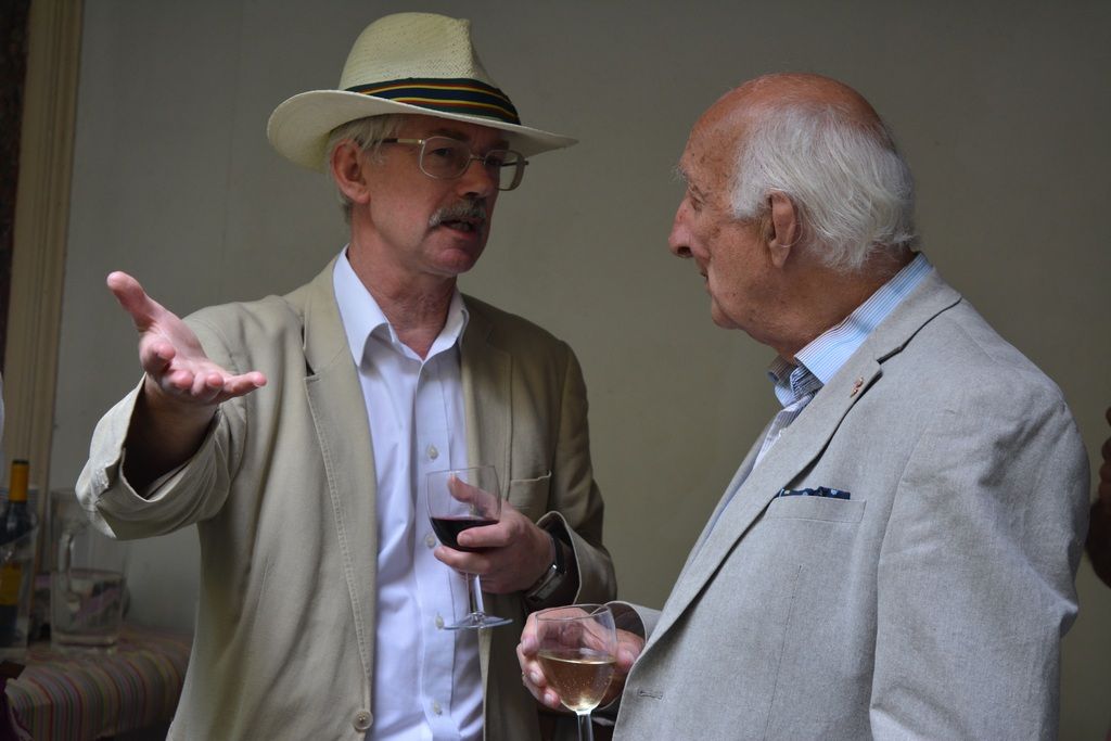 Two guests talking, one wearing a wide-brimmed hat.