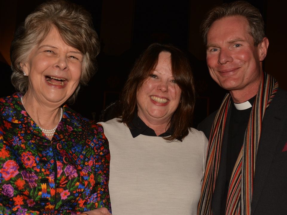 Three parishioners smiling together at an indoor gathering.