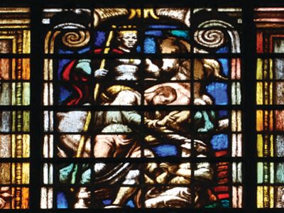 A stained-glass window with a central religious figure and ornamental borders.