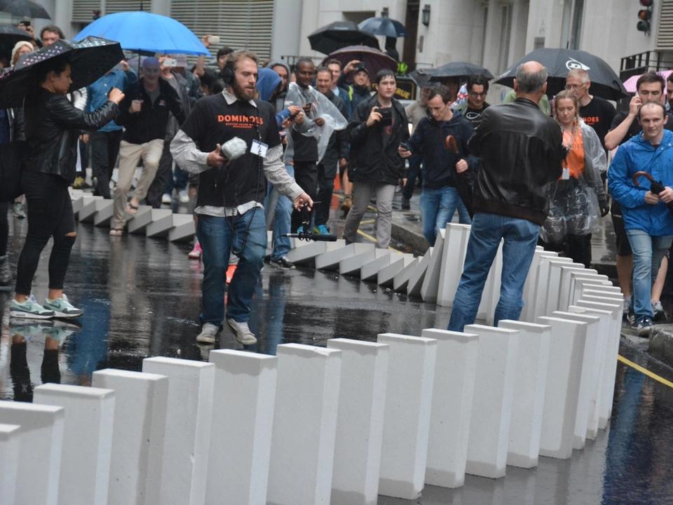 A crowd watching white blocks topple along a wet street.
