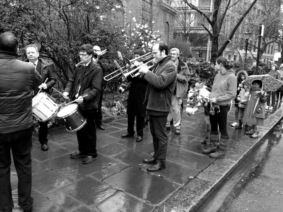 A drummer and wind players walking at the front of a street procession.