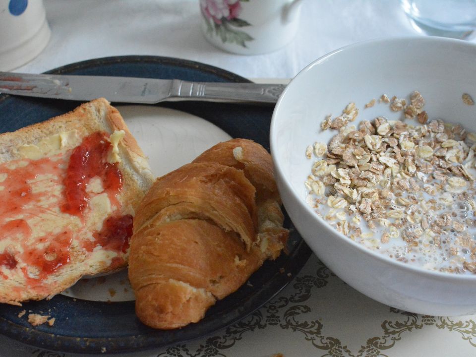Breakfast plates with toast, a croissant and a bowl of cereal.