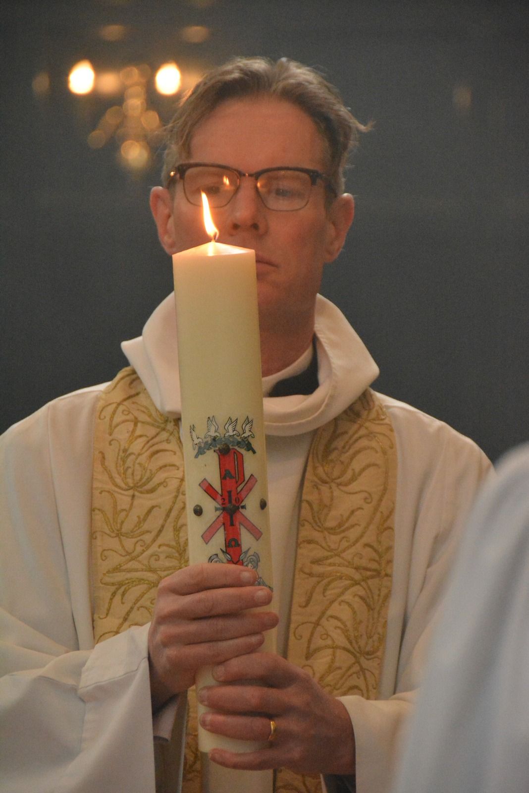 A priest holding a large decorated Easter candle.