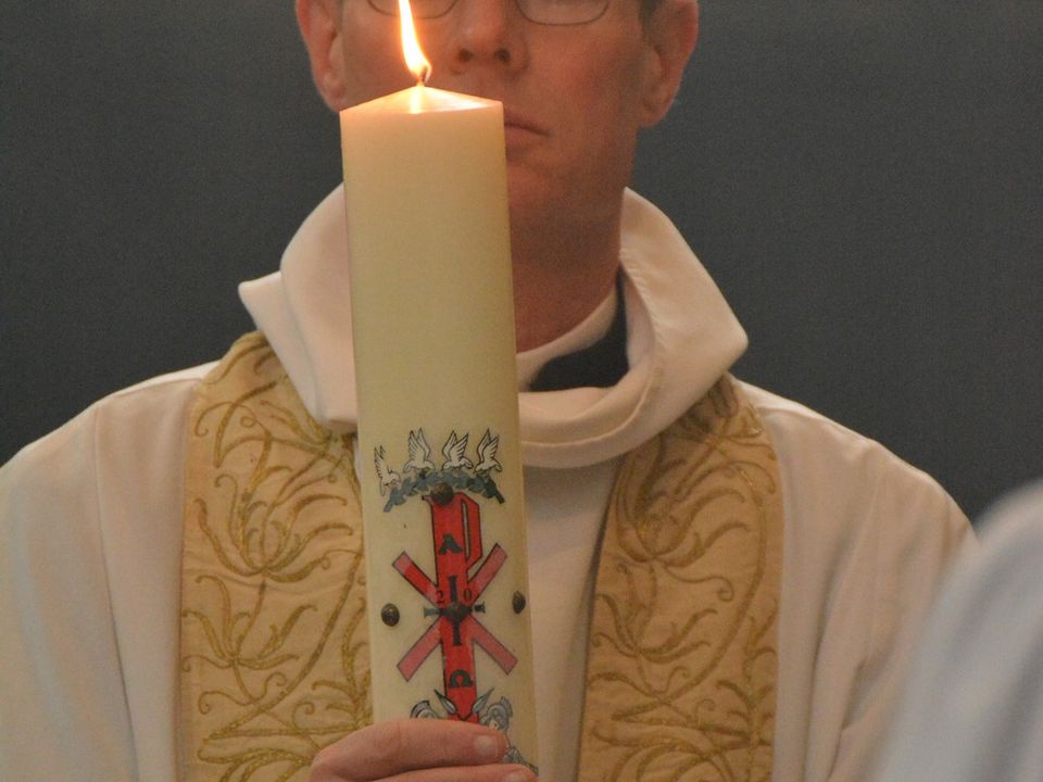A priest holding a large decorated Easter candle.