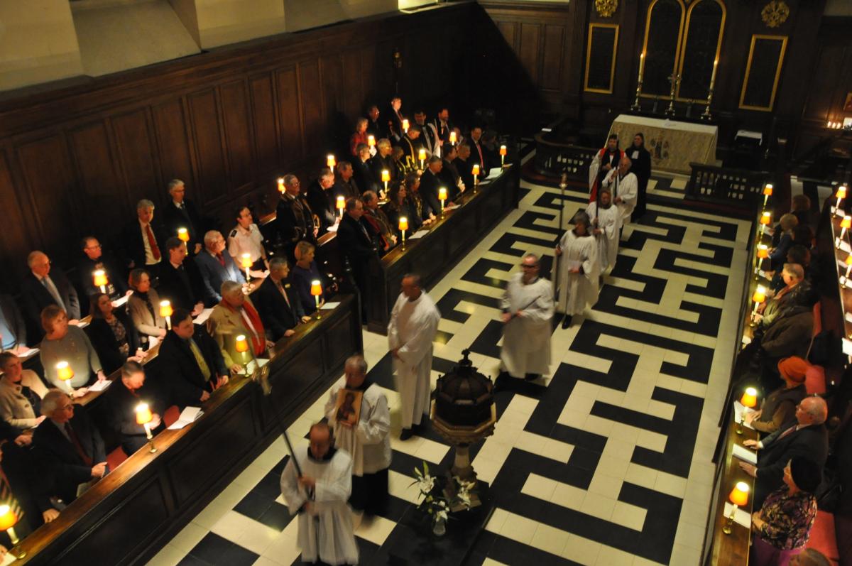 Clergy and congregation gathered around the central aisle during a candlelit service.