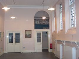 An empty church hall with high windows and pendant lights.