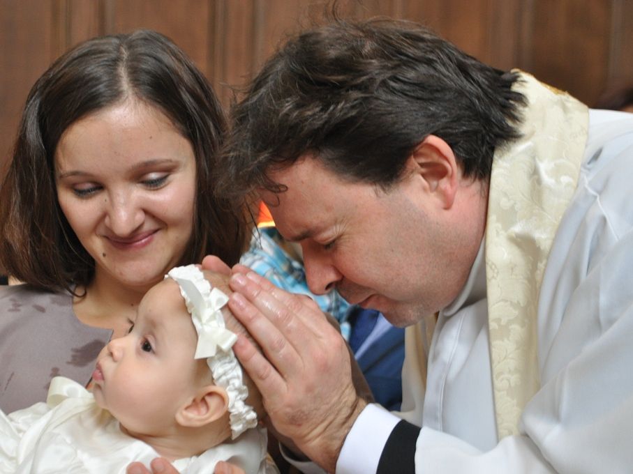 A close view of a priest and an adult holding a baby during baptism.