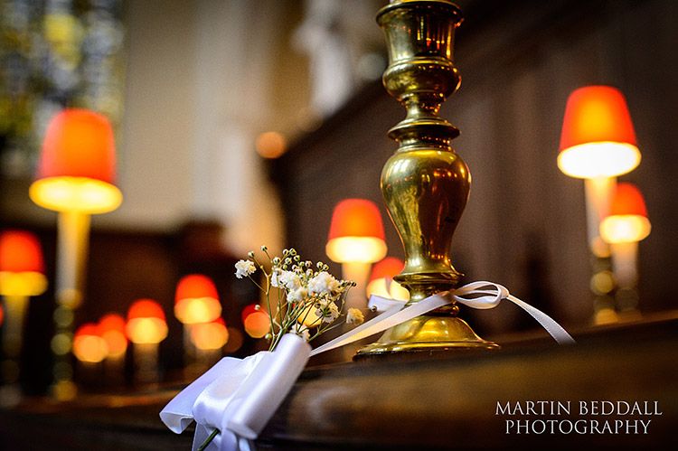 A small floral decoration and ribbon beside a brass lamp on a wooden pew.