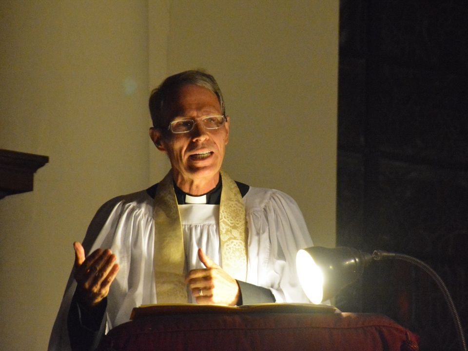 A speaker smiling and gesturing at the illuminated pulpit.